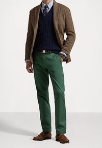 Brun kavaj med fiskbenmönster över en marinblå kabelstickad tröja, gröna byxor och bruna läderskor. Accessoarer inkluderar en armbandsklocka och slips.