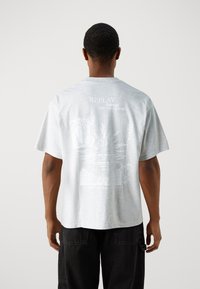 Camiseta gráfica de color gris claro, material de algodón, de manga corta, con cuello redondo; presenta texto en blanco y diseños intrincados en la parte trasera.