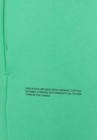 Grüne Shorts aus biologischer Baumwolle mit glatter Textur. Enthält bedruckten Text, der die Behandlung des Stoffes für Frische beschreibt.