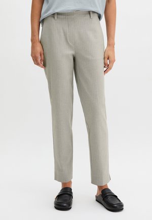 Pantaloni sartoriali grigi chiaro a righe sottili indossati con mocassini neri senza lacci, mostrati dalla vita ai piedi su una persona in piedi.