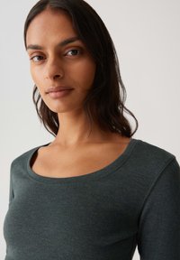 Donkergroene langemouwen shirt van zachte, rekbare stof met een ronde hals en eenvoudig ontwerp. Soepele textuur, getailleerde pasvorm.