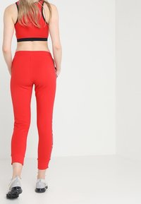 Czerwone sportowe legginsy z bocznymi paskami, dopasowany krój i miękka tkanina. Wykończone elastycznym paskiem w talii i zwężanym dołem. Szare obuwie.