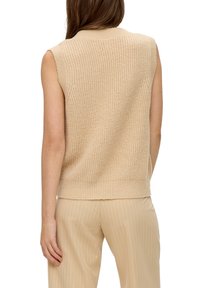 Beige mouwloze gebreide top met een gestructureerde afwerking en geribbelde zoom, gecombineerd met licht gestreepte hoge taille trousers.