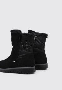 Botas negras hasta el tobillo, hechas de serraje y tejido, con un collar de piel sintética, un acento de estrella negra brillante y suela de goma texturizada.