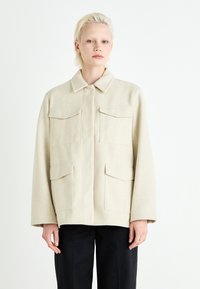 Beige ullblandingsjakke med fire frontlommer, krage og lange ermer. Stoffet har en myk tekstur og en strukturert design.