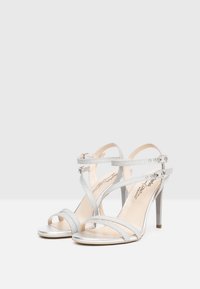 Sandali argentati con tacco, con più cinturini, realizzati in materiale luccicante. Presentano un design open toe e una fibbia regolabile alla caviglia.