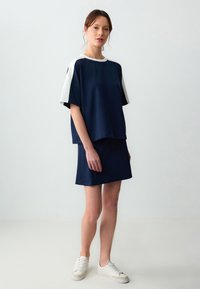 Top blu navy con maniche bianche abbinato a una gonna blu navy coordinata; texture liscia; vestibilità comoda; indossato con sneakers bianche.