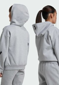 Sudadera con capucha gris de corte relajado, hecha de una tela suave. Presenta un bolsillo tipo canguro y un detalle del logo negro en la manga.