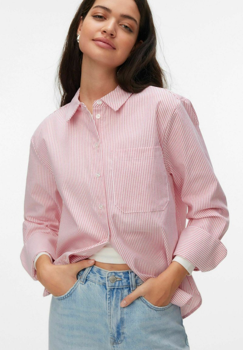 Chemise à boutons rayée rouge et blanche avec un col, une poche poitrine gauche et des manches retroussées, associée à un jean en denim bleu clair.