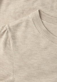 Primo piano di un maglione beige lavorato a maglia che mostra una scollatura a coste tonda e un dettaglio sottile di spalle leggermente arricciate su un tessuto morbido.