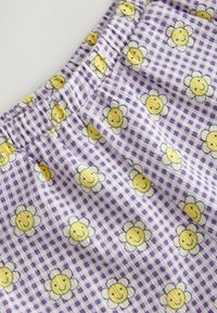 Lila Gingham-Stoff mit gelben Smiley-Blumen. Das Material ist weich, hat einen elastischen Bund und eine leichte, strukturierte Oberfläche.