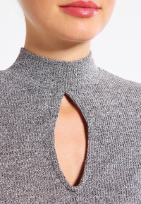 Grå ribbad tröja med hög krage och ett nyckelhål öppning framtill. Texturen verkar mjuk och kroppsnära.