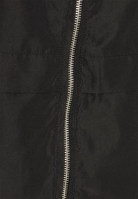 Černá bunda se stříbrným zipem, která má hladkou texturu látky a čistý design, zdůrazňující minimalistický styl a funkčnost.