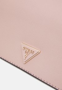 Růžový texturovaný syntetický materiál, zobrazující zlaté trojúhelníkové logo s raženým písmem, prošitými okraji a jemným, hladkým leskem.