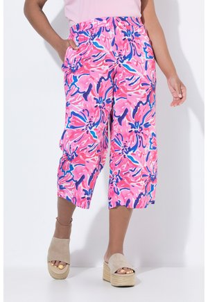 Vrouw draagt korte, wijde broek met roze, blauwe en koraalkleurige bloemenpatronen, gecombineerd met beige plateausandalen en gele nagellak.