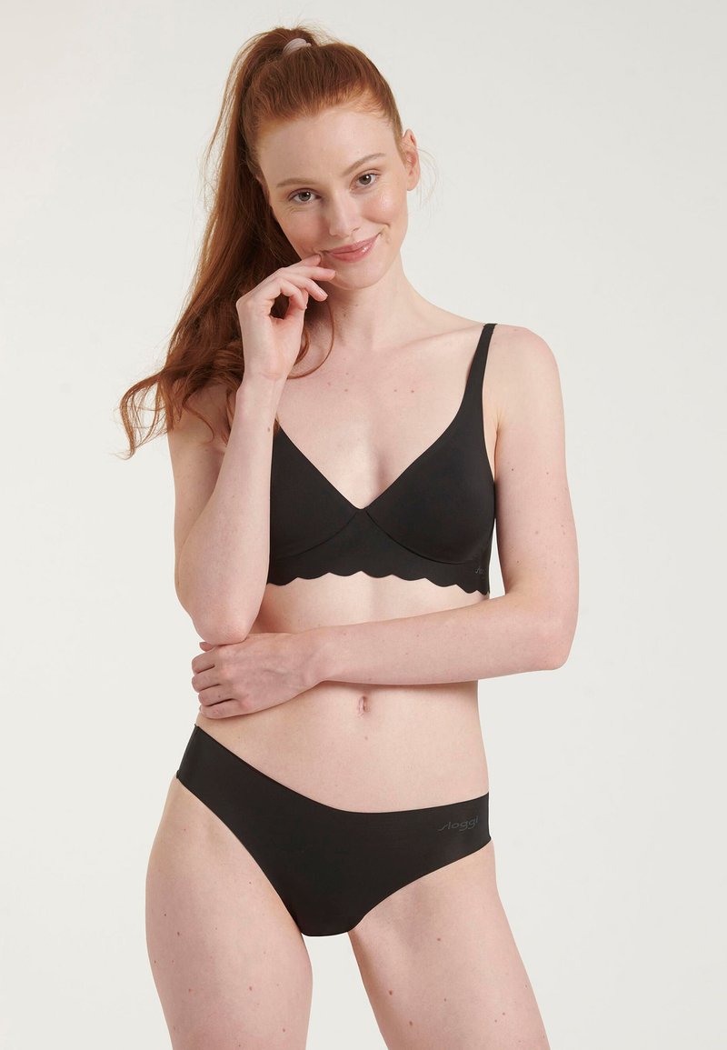 Ensemble de lingerie noire comprenant un soutien-gorge à bords festonnés et un slip assorti. Matériau lisse avec un design minimaliste et un détail logo sur le slip.