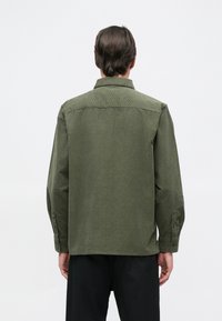 Camisa verde de botones, hecha de una tela texturada, con cuello y mangas largas, de corte recto y con puños abotonados.