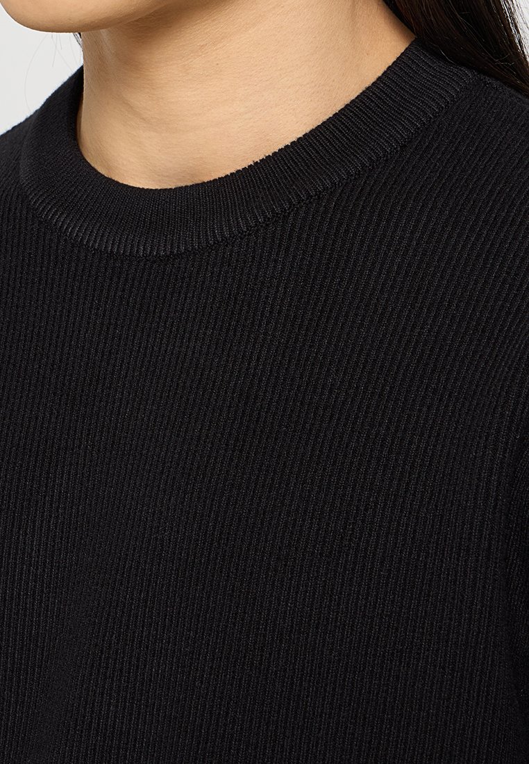 Maglione nero a costine con collo rotondo. La texture è morbida e strutturata, mettendo in evidenza il dettaglio delle costine verticali.