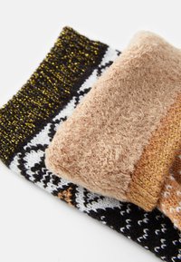 Τρία ζευγάρια κάλτσες με σχέδια: μαύρες με λευκά γραφικά σχέδια, μπεζ με χνουδωτή υφή και πορτοκαλί με λεπτές χρυσές κλωστές.