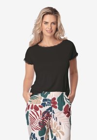 Czarny top z krótkimi rękawami z koronkowym wykończeniem, zestawiony z wzorzystymi jasnymi spodniami w liście w odcieniach zieleni, czerwieni i niebieskiego.