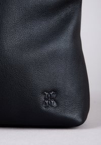Black leather bag with a textured surface, featuring a subtle embossed design at the bottom. Smooth, structured shape and soft finish.
