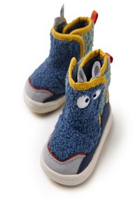 Botines azules con una textura esponjosa, que presentan acentos amarillos y verdes, recortes grises en las orejas y una lengüeta roja en el talón. Construcción de suela suave.