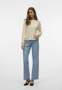 Maglione lavorato a maglia color crema con trama aperta, dalla vestibilità rilassata. Abbinato a jeans dritti blu chiaro e sandali neri con tacco.