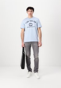 Tricou din bumbac bleu deschis cu logo imprimat negru, blugi din denim gri, adidași albi și o geantă tote neagră. Design simplu și croi lejer.
