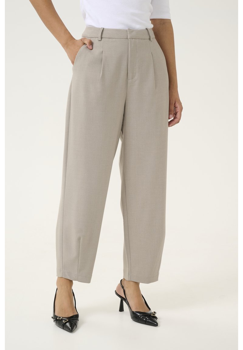 Beige, hoch taillierte Hose mit vorderen Falten, einer glatten Textur und schmal zulaufendem Bein. Kombiniert mit schwarzen, spitzen Absatzschuhen.