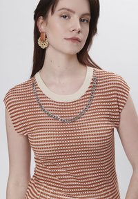 Teksturiseret kortærmet top i rust og creme striber, med en creme halsudskæring og sølv kædelys. Modellen bærer store perleøreringe.