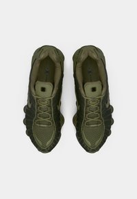 Mørkegrønne atletiksko med et mesh-overmateriale, strukturerede detaljer og afrundede såleegenskaber, designet til åndbarhed og støtte.