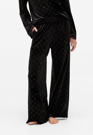 Zwarte fluwelen pyjamabroek met een subtiel patroon, wijde benen en een elastische tailleband met zijzakken. Zachte textuur, relaxte pasvorm.