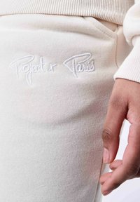 Pantalones de chándal grises en un suave tejido de punto con un logo bordado "Project + Paris". Incluye un bolsillo lateral y una cinturilla acanalada.