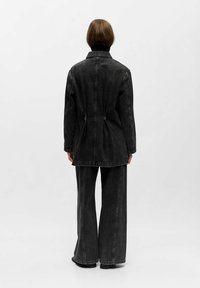 Zwarte spijkerjack met een nauwsluitende taille, lange mouwen en een kraag. Gecombineerd met losse zwarte spijkerbroek. Gevoed, casual ontwerp.