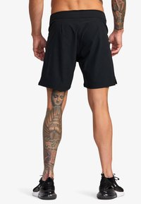 Sorte træningsshorts med elastisk talje, glat tekstur og afslappet pasform, parret med sorte løbesko med hvide accenter.