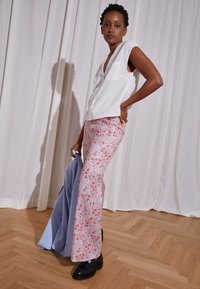 Blusa branca sem mangas com um decote em V, combinada com calças de padrão floral claro em rosa e azul, e sapatos de plataforma pretos.