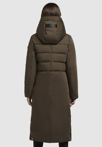 Lange bruine pufferjas met een hoge kraag en een oversized capuchon. Heeft een gewatteerd ontwerp, zijsplitten en een logo op de achterkant.