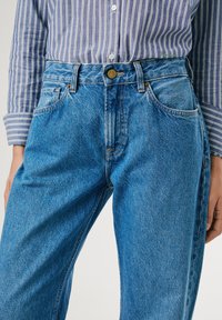 Light blue denim jeans with a high waist, five-pocket design, and subtle whiskering. Features a metal button and contrasting stitching details.