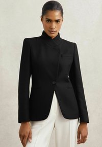 Kohandatud must bleiser kõrge kraega, tekstuuriga kangast, ühe nupuga kinnitamine ja küljetaskud, koos kreemjate pükstega.