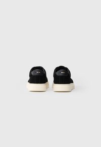 Et par svarte lavt opp sneakers med hvite såler vist fra baksiden på en enkel lys grå bakgrunn.