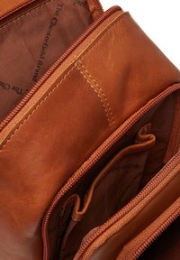 Interno di una borsa in pelle marrone con compartimenti con cerniera, caratterizzato da una texture liscia e cuciture a contrasto. La fodera presenta una stampa del marchio discreta.