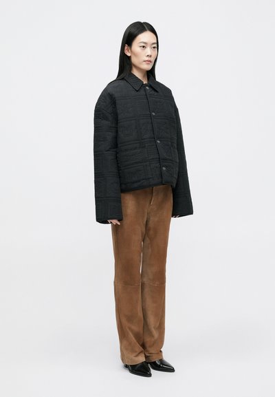 Musternahk kootud jakk kraega, nööbiga kinni ja laia varrukatega. Kantud pruunide puuvillaste pükste ja mustade terava ninaga kingadega.