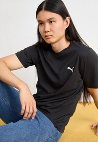 Černé bavlněné tričko s krátkým rukávem a kulatým výstřihem, s bílým logem Puma na levé části hrudi, spárované s modrými džínami.