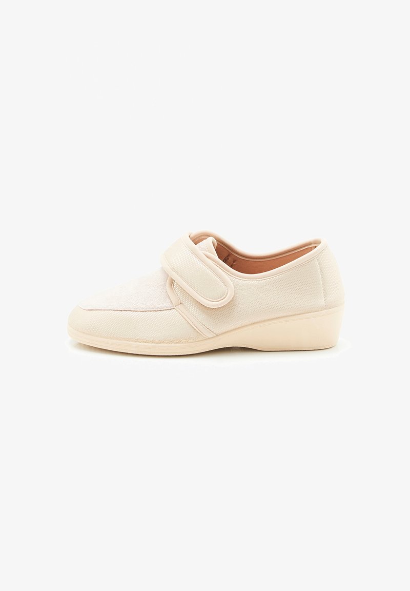 Beige stoffen schoen met een klittenbandsluiting, ronde neus en gestructureerde bovenkant. Lage wigzool zorgt voor een lichte verhoging.