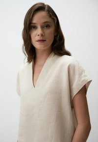 Beige linnen top met korte mouwen en een V-hals, voorzien van een textuurstof en een ontspannen pasvorm.