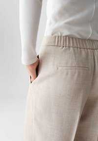Lichtbeige broek van een gestructureerde, geweven stof. Heeft een ontspannen elastische tailleband en een zijzak voor functionaliteit.