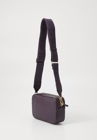 Purple leather crossbody bag with a rectangular shape, zip closure, and a textured strap featuring pattern accents. Gold hardware detailing.