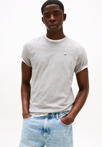 Grå bomulds-T-shirt med rund hals, hvide opsmøgede ærmekanter og lille logodetalje på brystet, kombineret med lyseblå denimjeans.