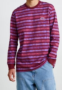 Långärmad skjorta i vinröd och lila randig mönster, tillverkad av mjukt material, med maroon ribbad halsringning och manschetter, prydd med en logo.