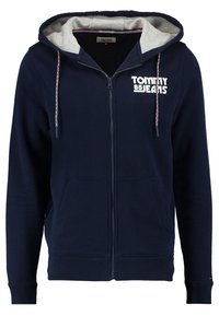 Felpa con zip di colore navy, con fodera della cappuccio grigia chiara, tasche frontali e testo del logo bianco sul petto. Coulisse regolabile con dettagli rossi.